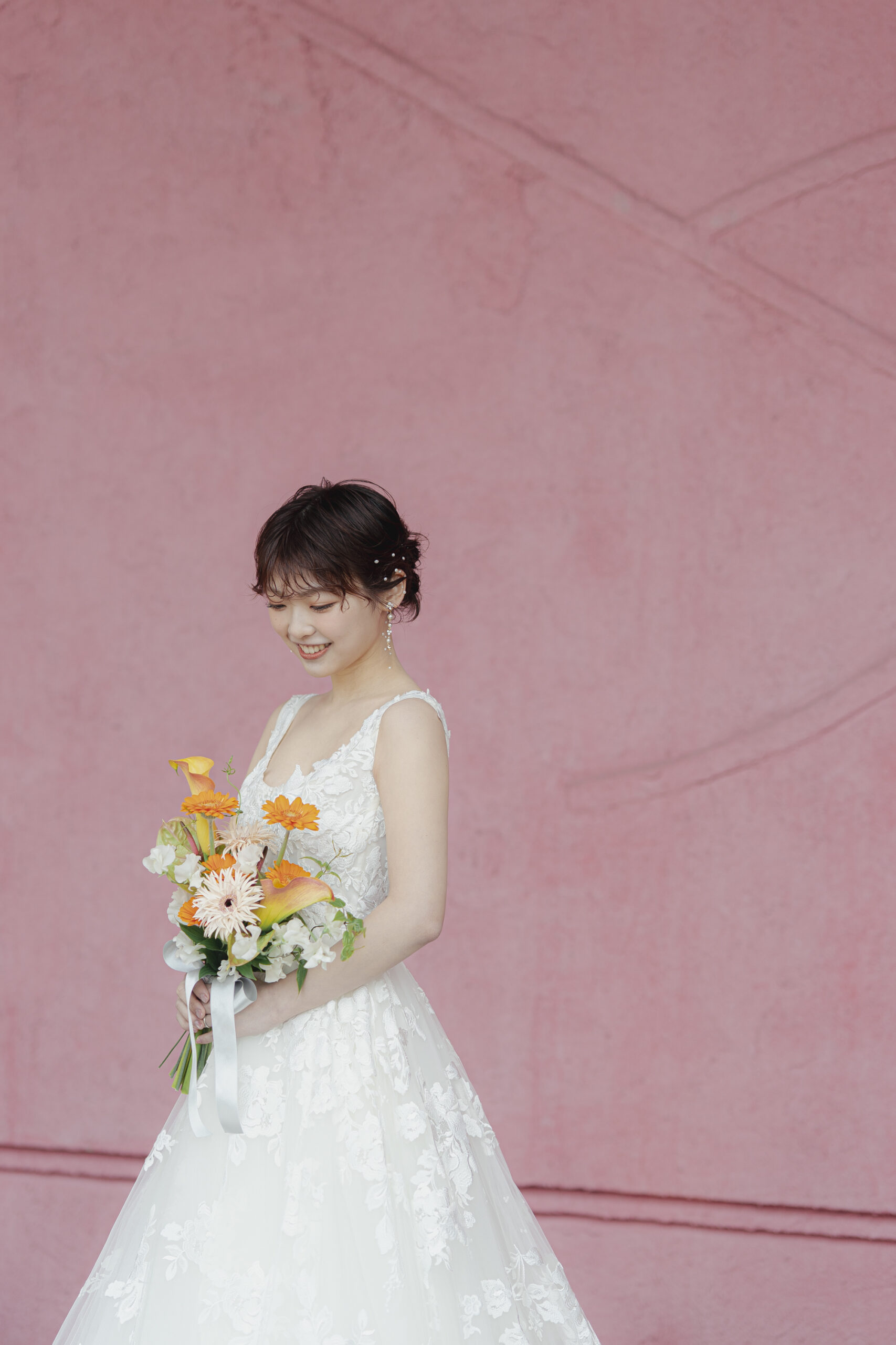 ザ・ルイガンズ スパ＆リゾートのピンクの壁の前で、ブーケを愛おしそうに見つめるご新婦様