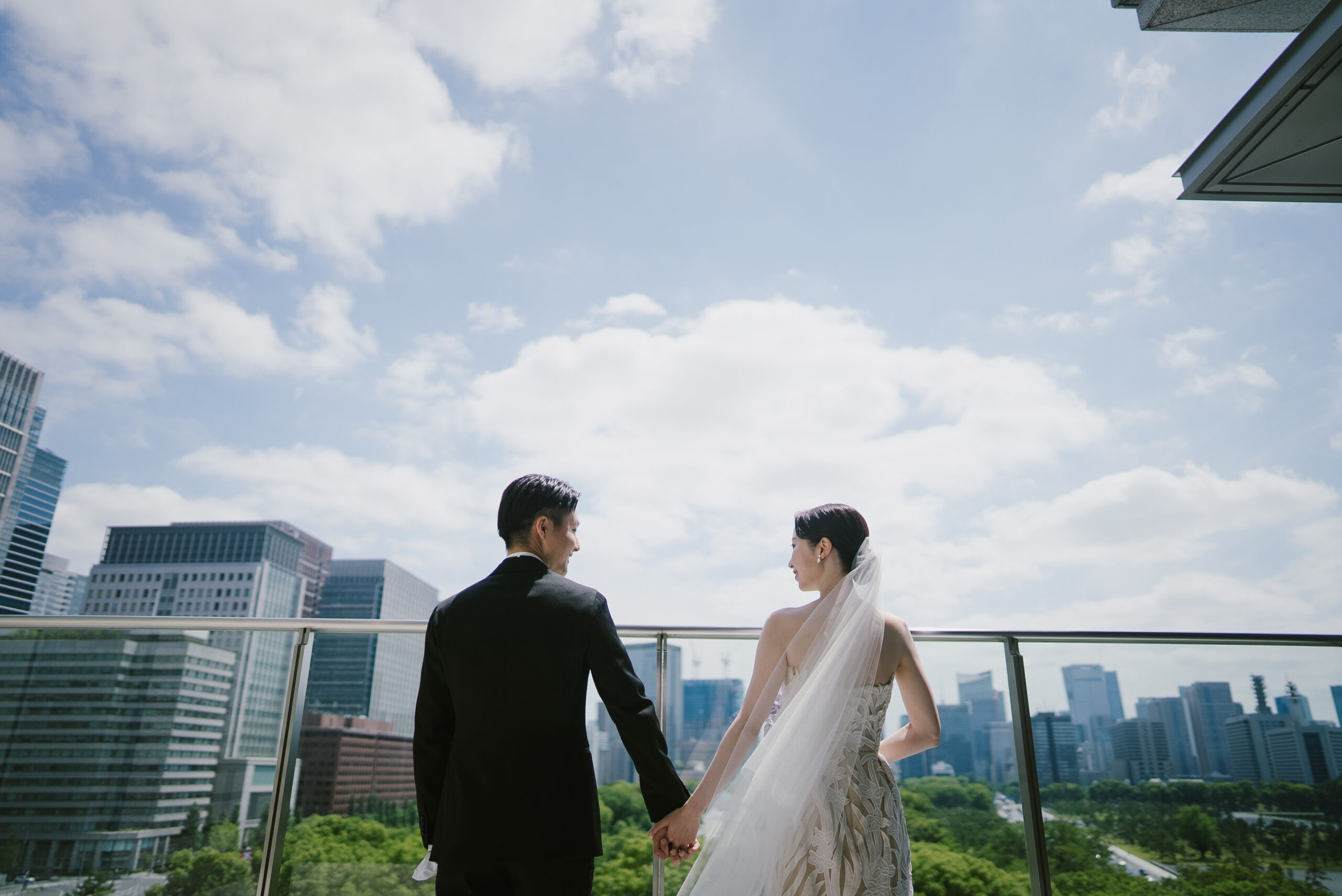 パレスホテル東京から臨む皇居の豊かな緑と大きな空を前に、ブラックタキシードに身を包むご新郎様と、花嫁に自信を与え美しさを引き立てるオスカーデラレンタのウェディングドレスを纏うご新婦様