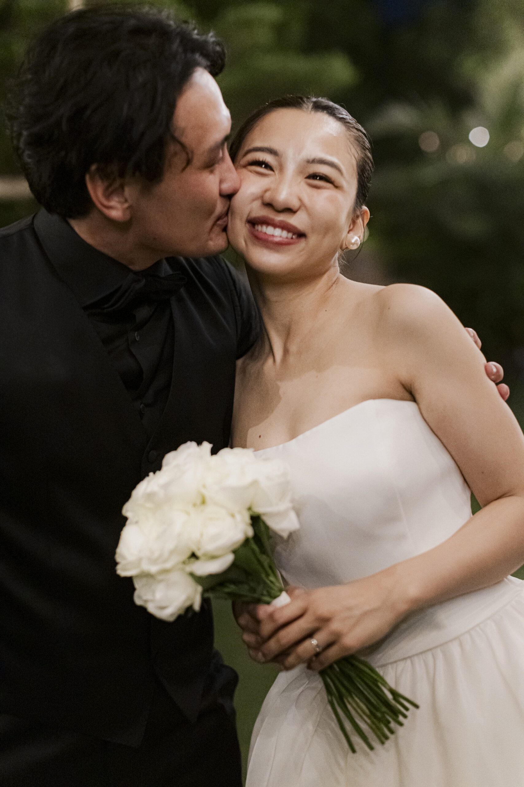 アムサーラのウェディングドレスを身に纏っているご新婦様にご新郎様が頬にキスをしている姿。